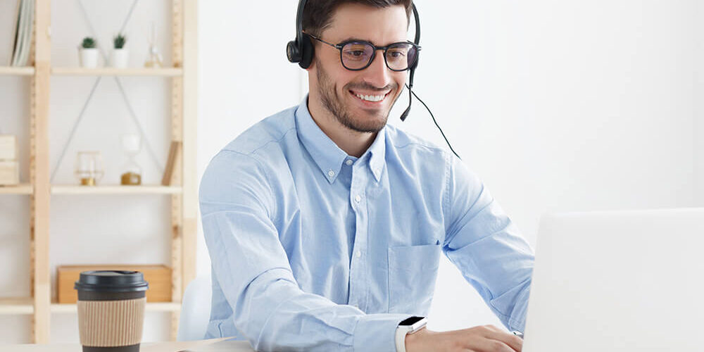 Mann sitzt lächelnd mit Headset am Laptop